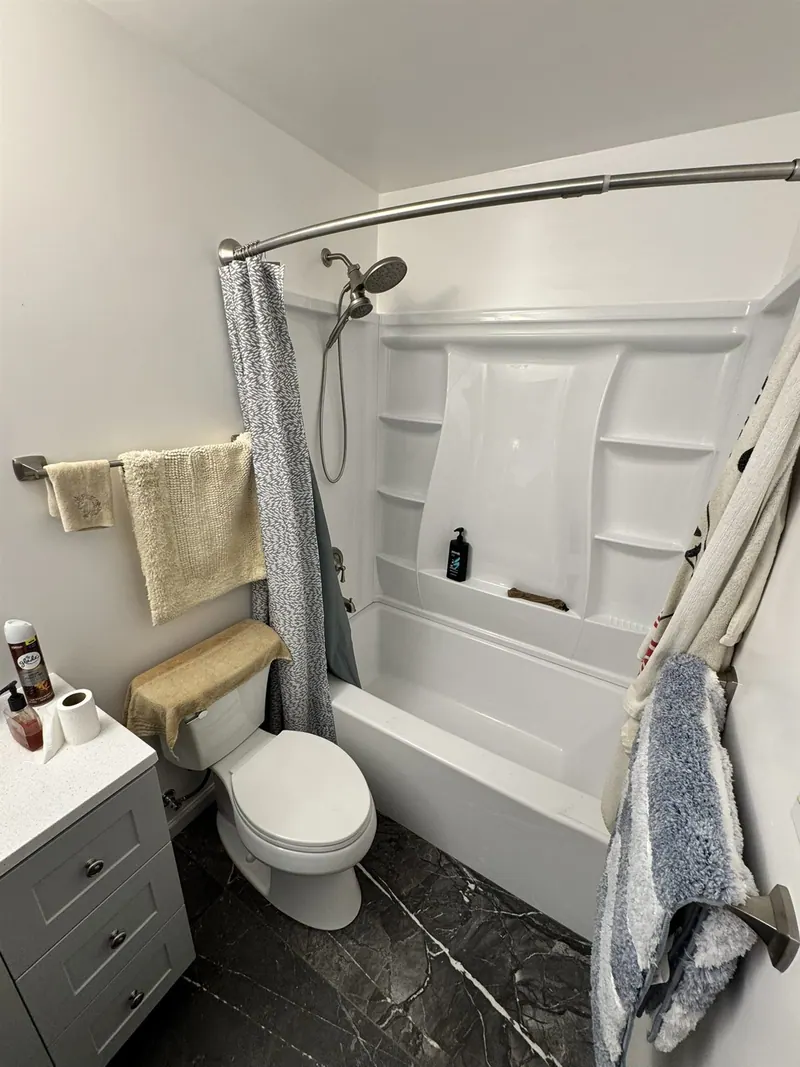 Compact bathroom with white tub surround, grey vanity and black marble-look floor