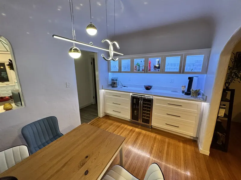 Built-in white buffet with wine fridge under a row of windows, pendant lights above the table
