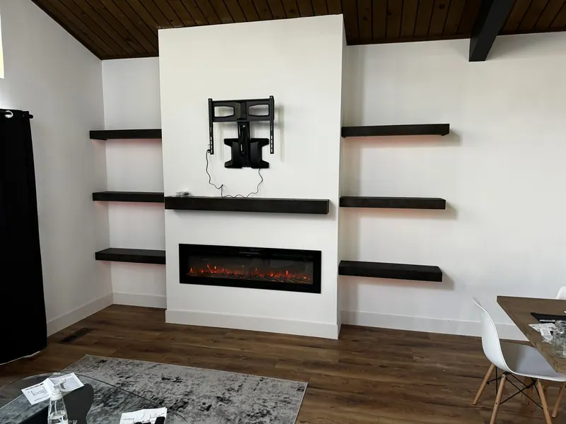 White fireplace wall with electric insert, dark floating shelves and a TV mount