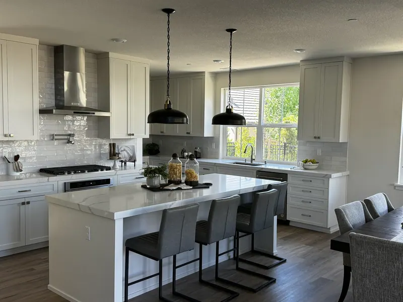 White shaker kitchen with a large island, black pendant lights and stainless range hood